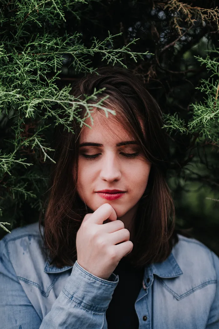 一位女士闭着眼睛站在云杉树下的照片