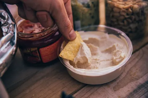 把玉米饼片浸在鹰嘴豆泥碗里放在桌上 把玉米饼片浸在鹰嘴豆泥碗里放在桌上