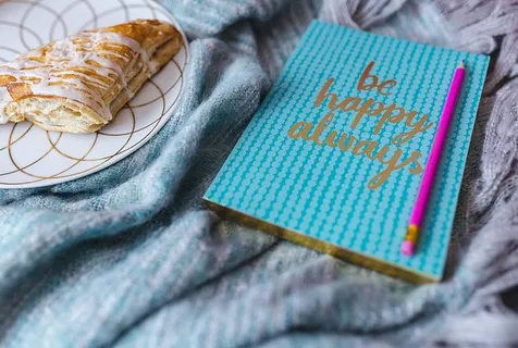 蓝色笔记本，带粉色iPhone、耳机和甜面包