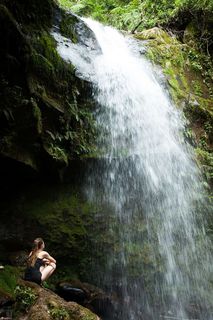 女子坐在岩石上面对瀑布的照片
