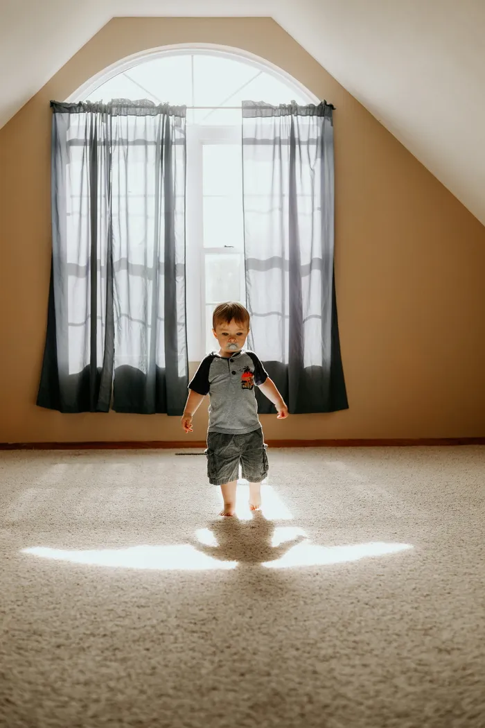 在白色粉刷的墙壁房间里，一个穿着灰色T恤和灰色短裤的男孩