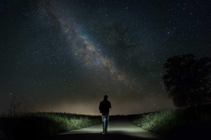 夜晚，一名男子在星空下的绿草间的水泥路上行走