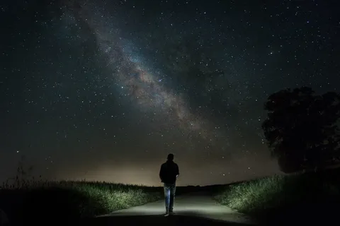 夜晚,一名男子在星空下的绿草间的水泥路上行走 夜晚,一名男子在星空下的绿草间的水泥路上行走