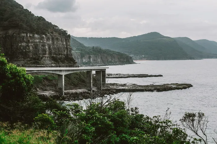 多云的天空下，海岸线上的山附近有一座混凝土桥