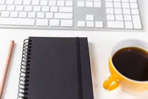 电脑键盘、咖啡杯、笔记本和铅笔放在一张白色的桌子上