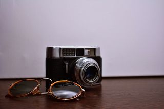 银色和黑色单反相机，棕色木质表面带棕色太阳镜