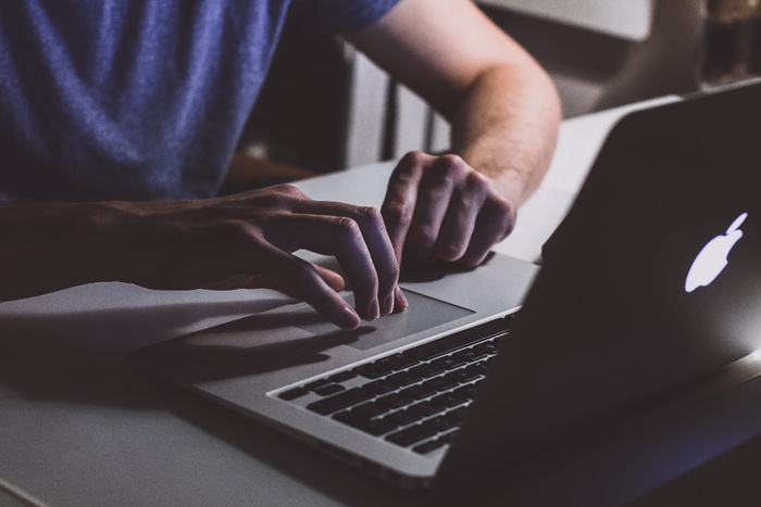触摸桌子上打开的Macbook的人