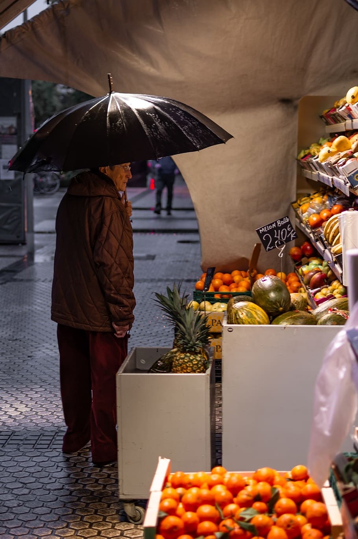 男子手持黑色雨伞站在水果摊前