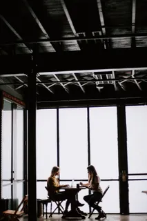 两个面对面的女人坐在靠近玻璃墙的桌子前的照片 两个面对面的女人坐在靠近玻璃墙的桌子前的照片