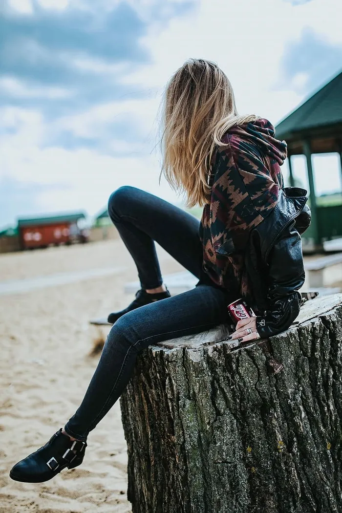 美丽的金发女人在海滩边的树桩上拿着一罐可乐放松