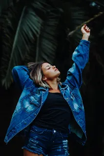 穿着蓝色水洗牛仔夹克和旧牛仔短裤的女士 穿着蓝色水洗牛仔夹克和旧牛仔短裤的女士