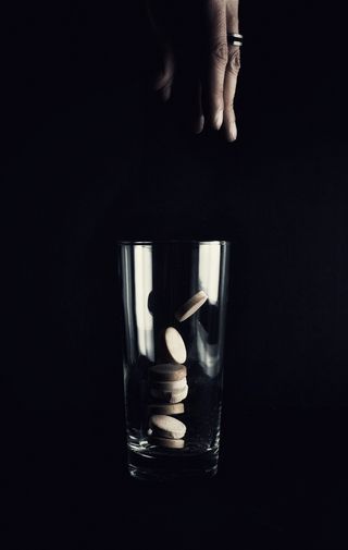 人们将药片滴在黑色表面的透明饮水杯上