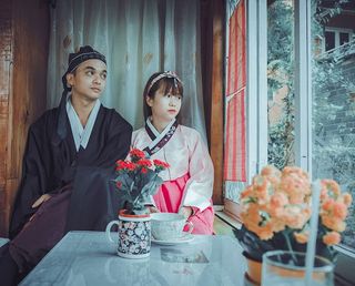 一对穿着韩国传统服装的情侣站在窗边盯着窗户