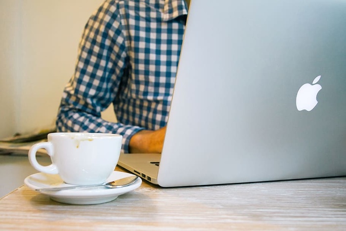 桌子上银色Macbook旁边的白色陶瓷茶杯