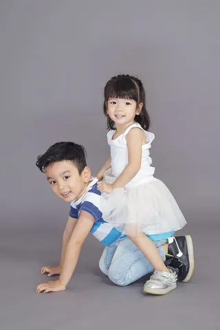 穿着白色连衣裙的女孩坐在爬行男孩的背上