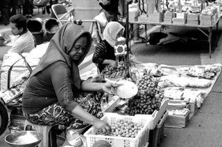 篮子里坐在水果旁边的女人的灰度照片