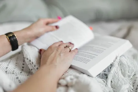 床上女人手拿书和咖啡的软照片