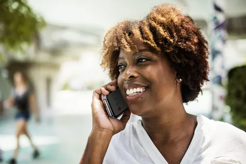 微笑的女人穿着白色V领衬衫，手里拿着灰色智能手机