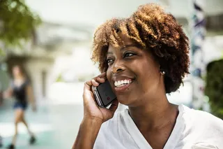 微笑的女人穿着白色V领衬衫，手里拿着灰色智能手机