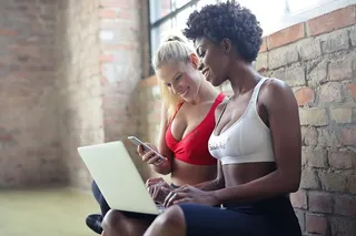 两名身穿红白运动胸罩的年轻女子在有氧舞蹈课上使用笔记本电脑和手机