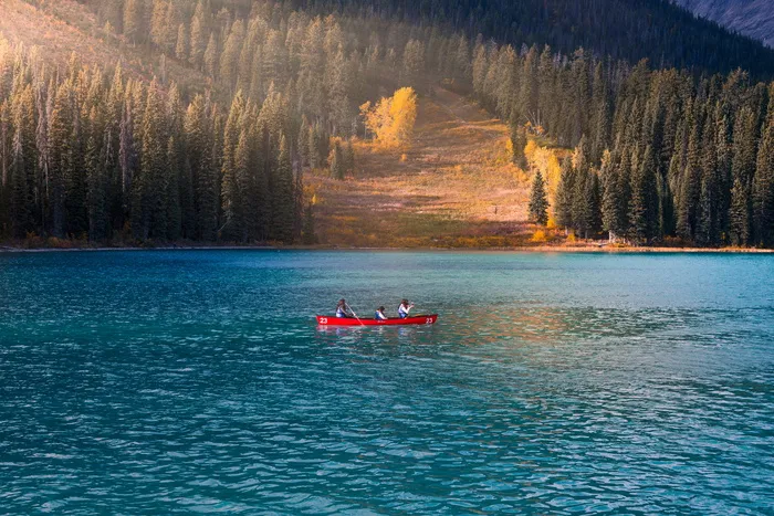 白天，三个人坐在蓝色平静的水面上的红色划艇上