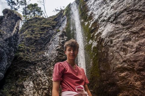 身穿红色圆领衬衫的男子站在瀑布附近