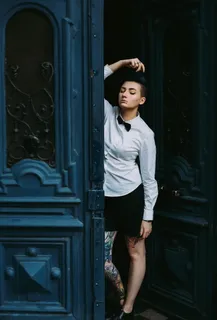 身穿白色衬衫、打着领结的女子倚靠在蓝色木门上 身穿白色衬衫、打着领结的女子倚靠在蓝色木门上