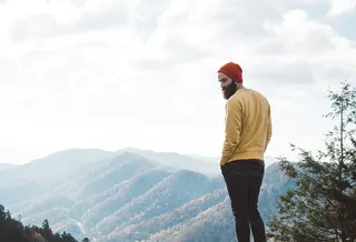 一个留着胡子戴着帽子的男人在山边