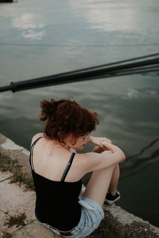 身穿黑色迷彩上衣的女子坐在靠近水体的混凝土表面上