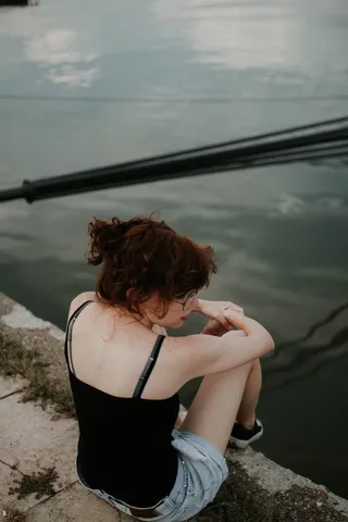 身穿黑色迷彩上衣的女子坐在靠近水体的混凝土表面上