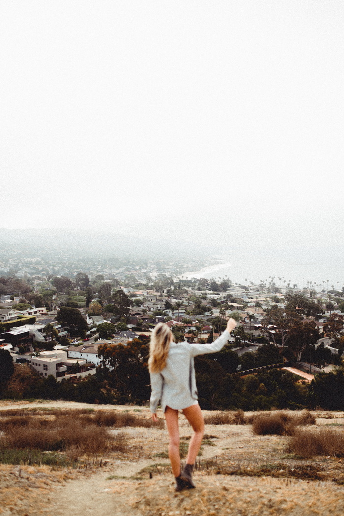 身穿白色上衣的女子站在棕色田野上俯瞰小镇