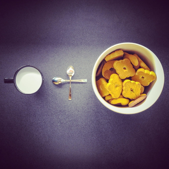 饼干放在两个不锈钢汤匙和黑色陶瓷杯附近的圆形白色陶瓷杯中