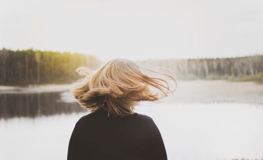 一名女子在看湖水时翻转头发的后视图照片