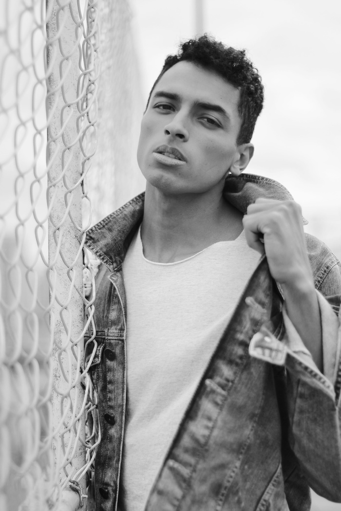 身穿牛仔夹克的男子站在链式围栏旁的灰度照片