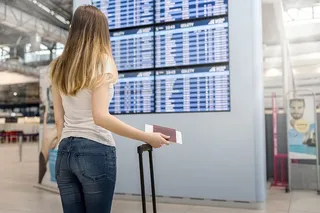 机场航班时刻表附近带着行李的年轻女子