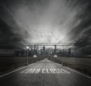 城市前面有灰色栅栏门的道路上封闭道路的灰度照片