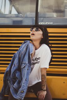 一名女子坐在黄色巴士保险杠上，手里拿着蓝色牛仔夹克