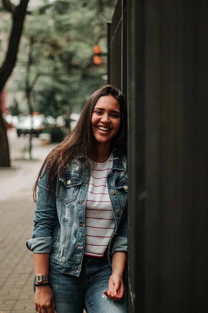 身着蓝色牛仔装的笑妇倚在金属栅栏上的照片