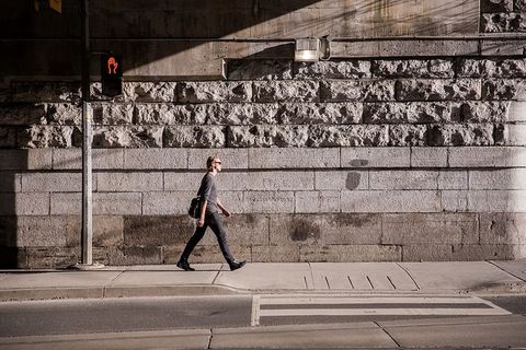 一个年轻的白人男子提着一个垃圾袋在城市的阳光下行走