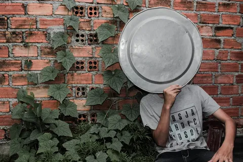 穿着灰色圆领T恤的人在砖墙旁边的脸上拿着托盘