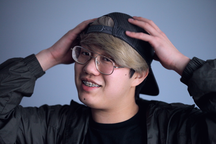 微笑的男子身穿黑色夹克，戴着黑色帽子，双手放在头上