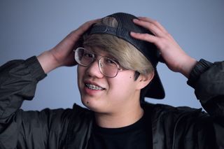 微笑的男子身穿黑色夹克，戴着黑色帽子，双手放在头上