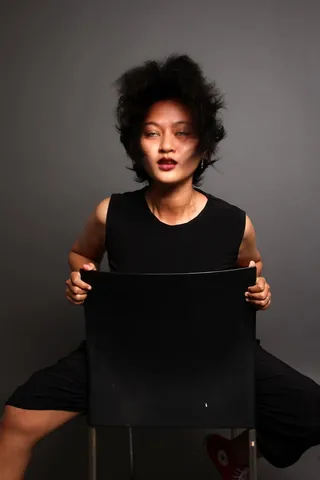 女人向后坐在灰色背景的黑色椅子上