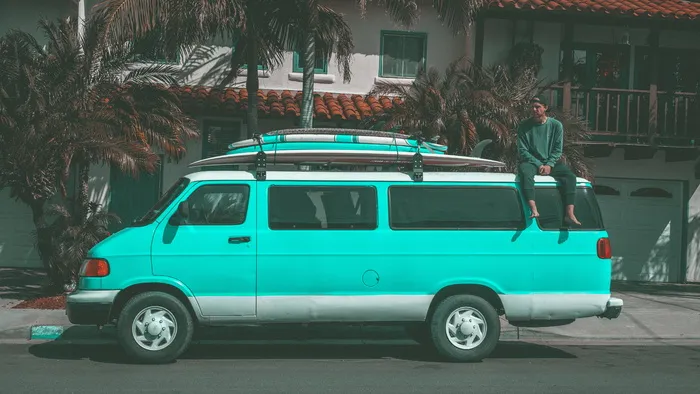一名男子坐在停在房子附近的Teal Dodge Ram面包车上