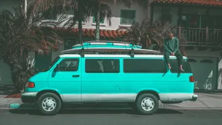 一名男子坐在停在房子附近的Teal Dodge Ram面包车上