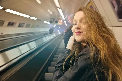 穿着黑色皮夹克的金发女郎在使用自动扶梯时回头看