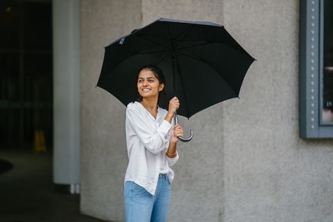 身穿白色长袖衬衫和蓝色牛仔裤的女子手持黑色雨伞的照片