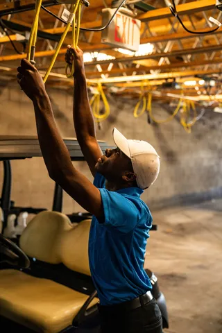 一个戴着白色帽子、穿着蓝色衬衫的男人伸手去抓一根黄色的绳子