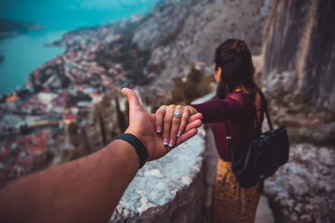 白天,女人牵着男人的手,看着水体旁的建筑物风景 白天,女人牵着男人的手,看着水体旁的建筑物风景