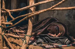 一名男子躺在地板上，身上盖着细条纹毯子